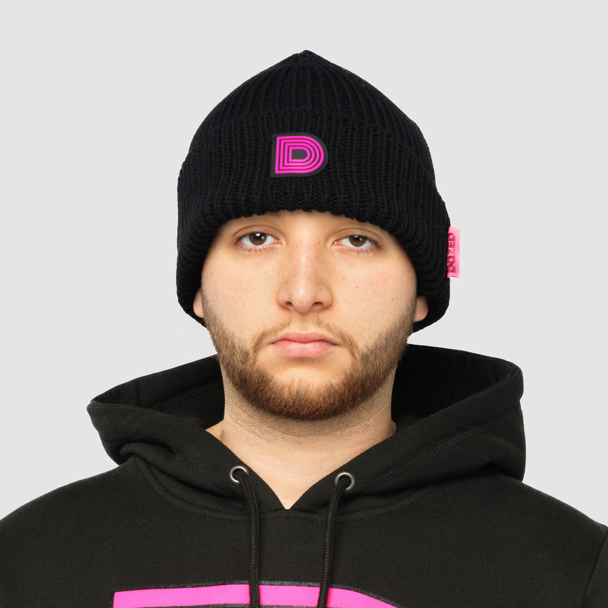 Product photo of a black skully hat with a pink D logo.
