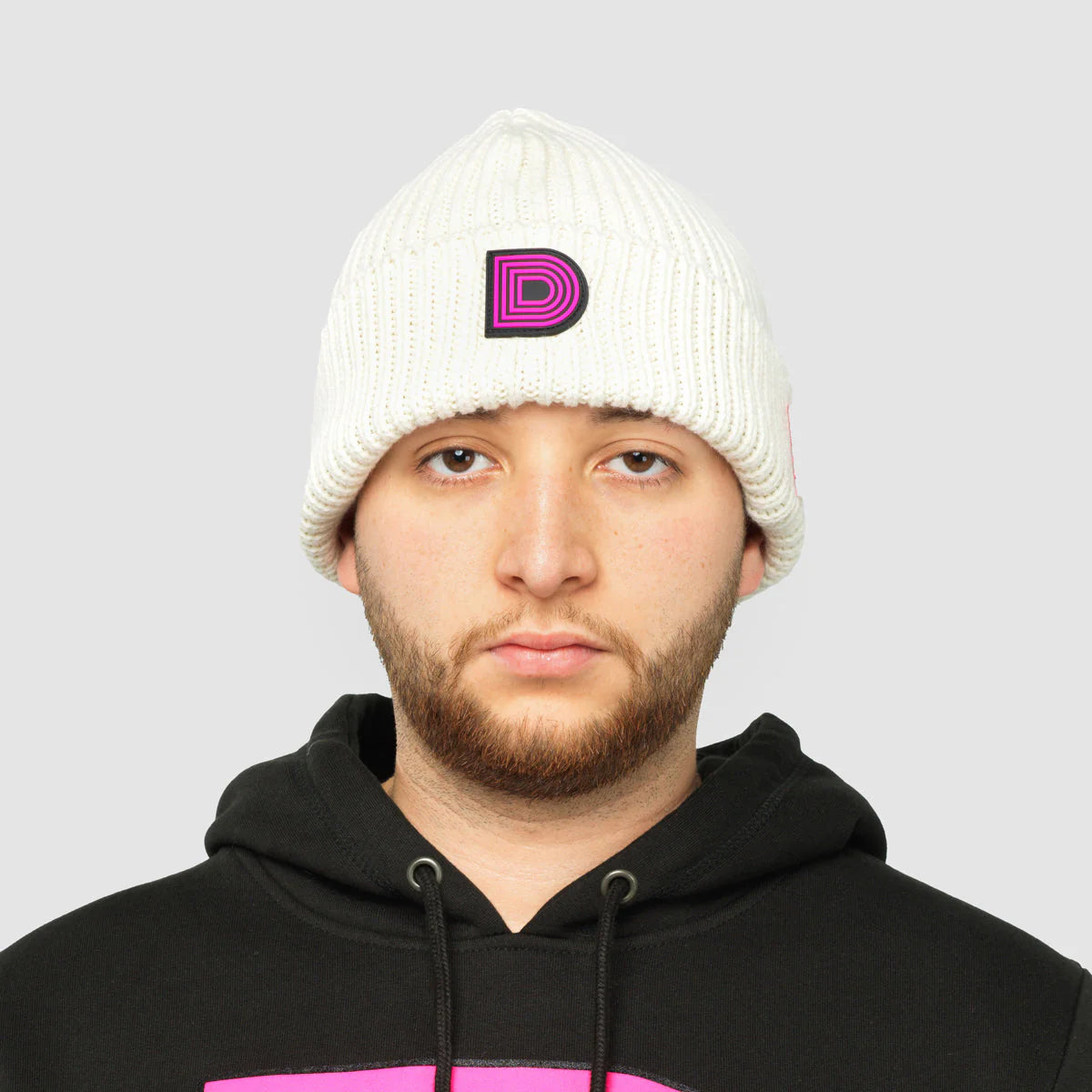 Product photo of a white skully hat with a pink D logo.