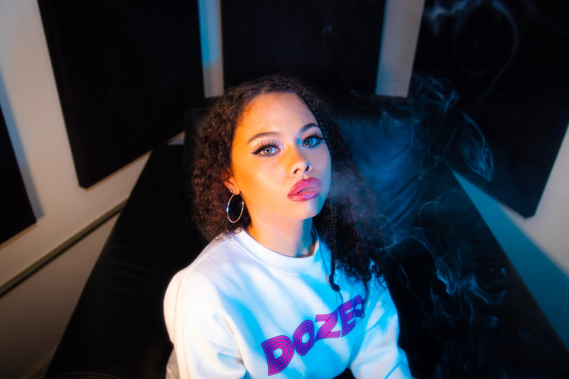 Product photo of a white sweater with prominent pink D logo.