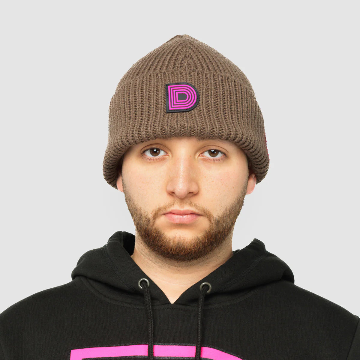Product photo of a brown skully hat with a pink D logo.